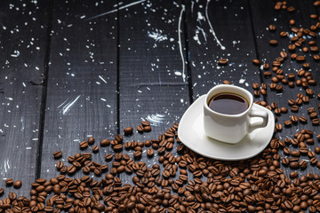 coffee pours into a Cup on a black wooden table with coffee beans.