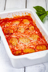 Wall Mural - Meatballs with tomato and sour cream sauce in white casserole dish on wooden background. Close up