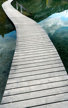 Long Curved Wooden Boardwalk And Footpath Over A Blue Mountain Lake With Reflections In The Water
