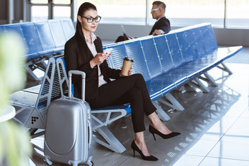 Wall Mural - young businesswoman in glasses using smartphone in departure lounge at airport