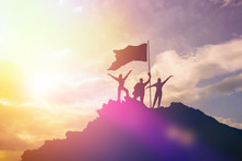 High Achiever, Silhouettes Of Three People Holding On Top Of A Mountain To Raise Their Hands Up. A Man On Top Of A Mountain. Conceptual Design. Against A Dramatic Sky With Clouds At Sunset.