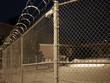 © Showtime Networks - Close up of a chain link barbed wire fence in front of a yard at night