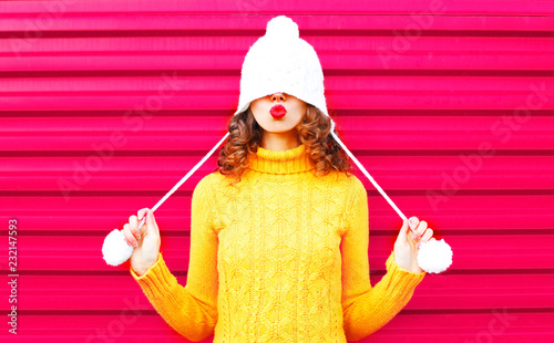 Fotografía Cool girl blowing red lips makes air kiss wearing colorful knitted hat, yellow s