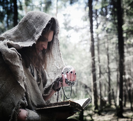 Fairy magician. A sorcerer with a glass sphere, a magical spell and a ritual. Elder with a staff and a cross in the forest. Black and white magic. A spell in an old book.