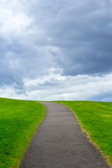 Poster - Natural background with a path up the hill, green grass and clouded sky