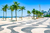 Bright morning view of the curving boardwalk tile pattern with palm trees at Copacabana Beach with the skyline of Rio de Janeiro, Brazil