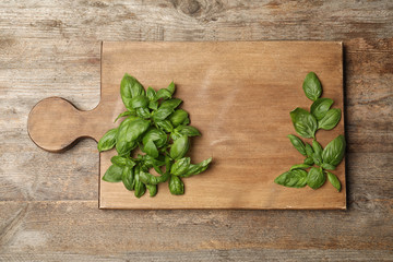 Board with fresh basil on wooden background, top view. Space for text