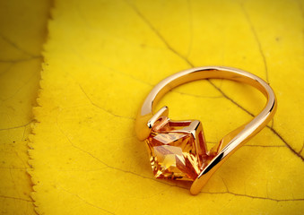 Jewelry ring with gemstone on yellow leaves background, copy space