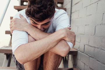 depressed young adult man hugging himself and sitting alone, mental illness health concept