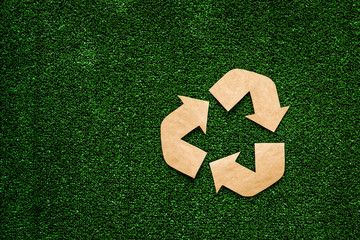 Wall Mural - Eco recycle sign made of craft paper on green grass background top view copy space