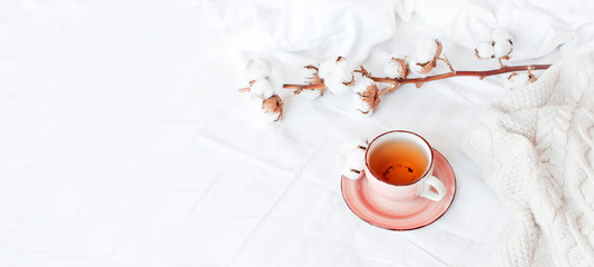 Wall Mural - Cup of hot tea, branch of delicate cotton and knitted plaid sweater in bed with white linens. Cozy morning breakfast at home. Lifestyle gentle female background Copy Space autumn winter concept