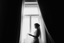 Gorgeous Beautiful Bride Silhouette In Silk Robe Under Veil Posing At Window. Happy Stylish Bride Standing In Soft Light. Bridal Morning