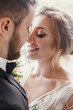 © sonyachny - Gorgeous bride and stylish groom gently hugging and embracing at window light. Sensual wedding couple smiling in light. Happy romantic moments of newlyweds. Wedding photo