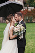 © sonyachny - Gorgeous bride and stylish groom passionately kissing under umbrella in rainy outdoors. Sensual wedding couple embracing. Romantic moments of newlyweds. Modern wedding photo