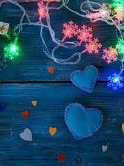 Two large handmade felt hearts and a few small ones made of colored paper, Christmas tree garlands of snowflakes on a blue textured wooden background, top view, concept of winter seasonal holidays