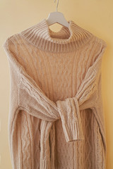 Wall Mural - One beige pastel knit warm sweater with knotted sleeves on hanger.