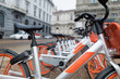 Rental bikes parked in a row on the square. The orange and silver bicycles are from Mobike, a company that guarantees service throughout the city. bicycle sharing system 