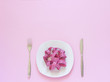 Pink measuring tape lying on plate in the form of spaghetti, knife and fork on pink background. Diet or anorexia concept. Top view Copy space