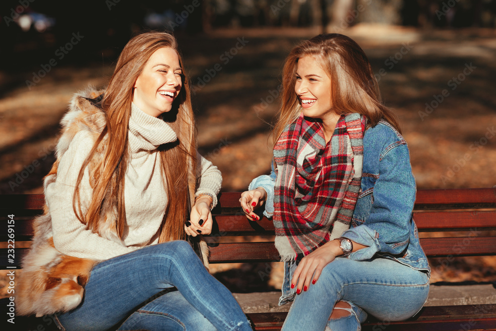 Two young women sitting on a bench in the park and laughing Stock Photo ...