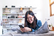 Pretty asian woman with glasses lying on the bed reading good news on line in a smart phone, woman lifestyle