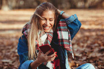 Young woman in the park using smartphone  and laughing