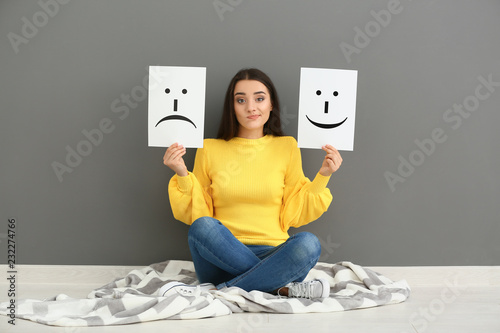 Cuadros en Lienzo Emotional woman holding sheets of paper with drawn emoticons while sitting near
