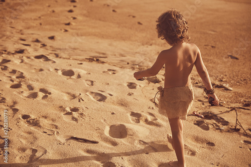 Fotomural Little mowgli boy walking on sand beach. Sunset light