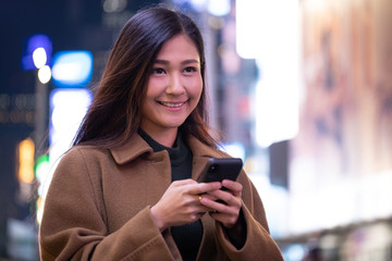 Canvas Print - Young Asian woman in city at night texting on cell phone