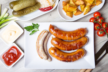 Grilled sausages with potatoes, cucumbers and sauerkraut, with two sauces. Close-up, selective focus.