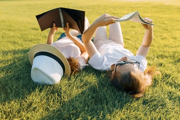 Top view, two young female students reading books lying on green grass