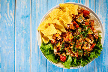 Grilled chicken meat with nachos and vegetables on wooden background