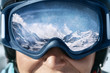Close up of the ski goggles of a man with the reflection of snowed mountains.  A mountain range reflected in the ski mask.  Man  on the background blue sky. Wearing ski glasses. Winter Sports.