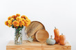 © NesolenayaAleksandra - Different multicolored decorative pumpkins, wooden plates or dishes and vase with yellow chrysanthemums flowers on a wooden table on a background of white wall. Autumn or fall home interior decor.
