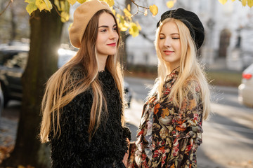 Two pretty girls walk on the city street, talk and smile to each other