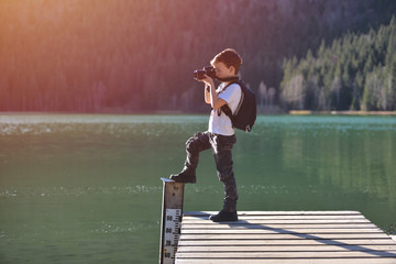 Creative child, kid photographer (a little boy) with a camera taking landscape pictures near la lake