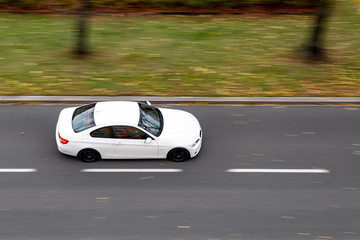 Very quickly driving white sports German coupe on a city street