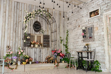 A Vintage Room  With A Iron Arch With Fake Window On A Wooden Wall And A Iron Table And Chairs On Another Brick Wall Surrounded By Flowers