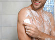 © New Africa - Young man taking shower with soap in bathroom, closeup. Space for text