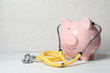 Piggy bank with stethoscope on light table. Space for text