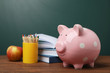 Piggy bank with stack of books and apple on table