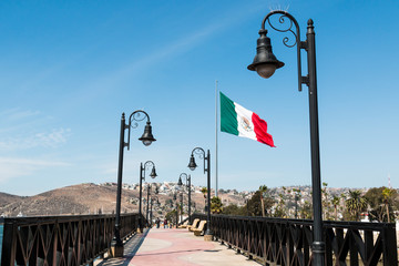 Pedestrian bridge leading to the marina and waterfront shops in Ensenada, Mexico, with a giant flag of Mexico.