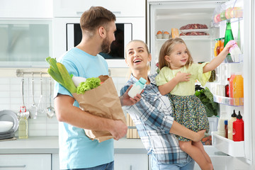 Happy family putting products into refrigerator in kitchen
