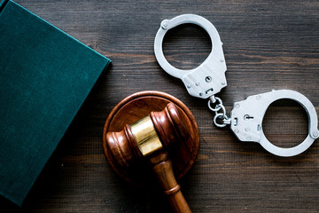 Crime concept. Metal handcuffs near judge gavel and law book on dark wooden background top view