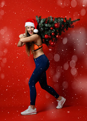 sexy Christmas fitness sport woman wearing santa hat holding xmas tree on her shoulders. snowflakes