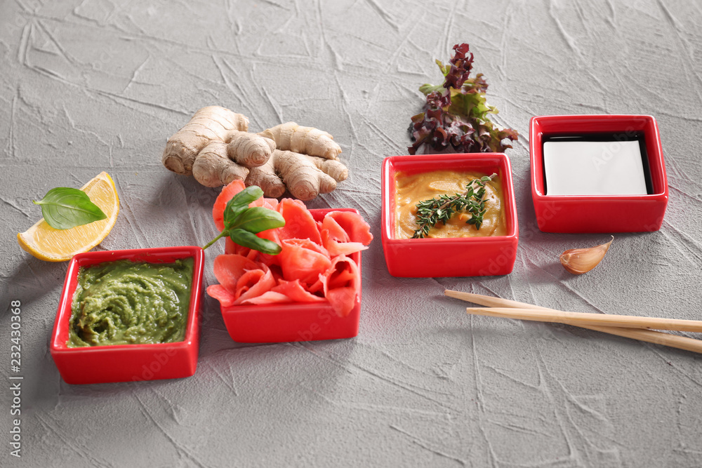 Different tasty sauces with marinated ginger in bowls on grey background
