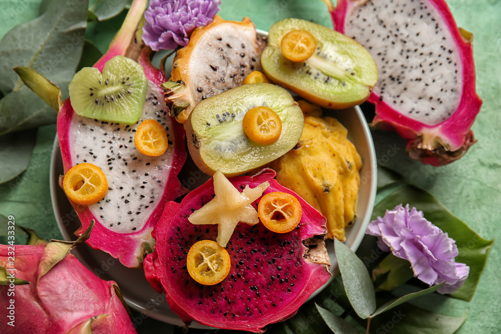Plate with pitahaya and other fruits on color background