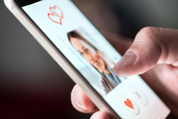 Online dating app in smartphone. Man looking at photo of beautiful woman. Person swiping and liking profiles on relationship site or application. Single guy searching for love partner. Mockup website.