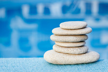 White Flat Rough Stones For Spa On Blue Blurred Background Towel And Pool. With Green Leaves Herbs. Zen Pyramid Balance.