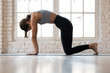 © fizkes - Young sporty attractive woman practicing yoga, doing asana paired with Cow Pose on the inhale exercise, Cat, Marjaryasana pose, working out, wearing sportswear, indoor full length, white yoga studio