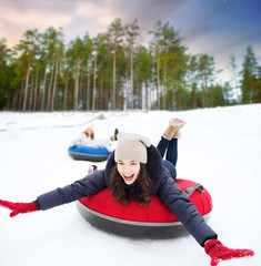 Sticker - winter, leisure and entertainment concept - happy teenage girl sliding down hill on snow tube over natural background